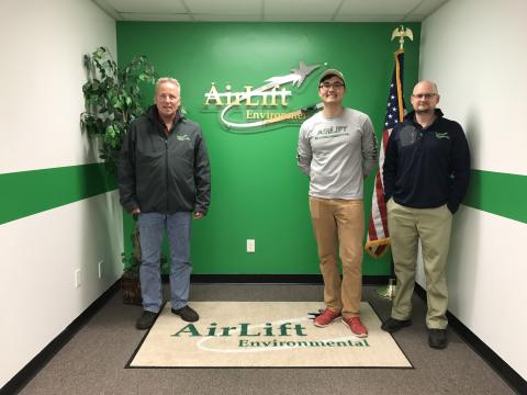 Three people standing in front of wall with AirLift logo