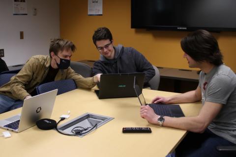 Three people working together at table looking at laptop